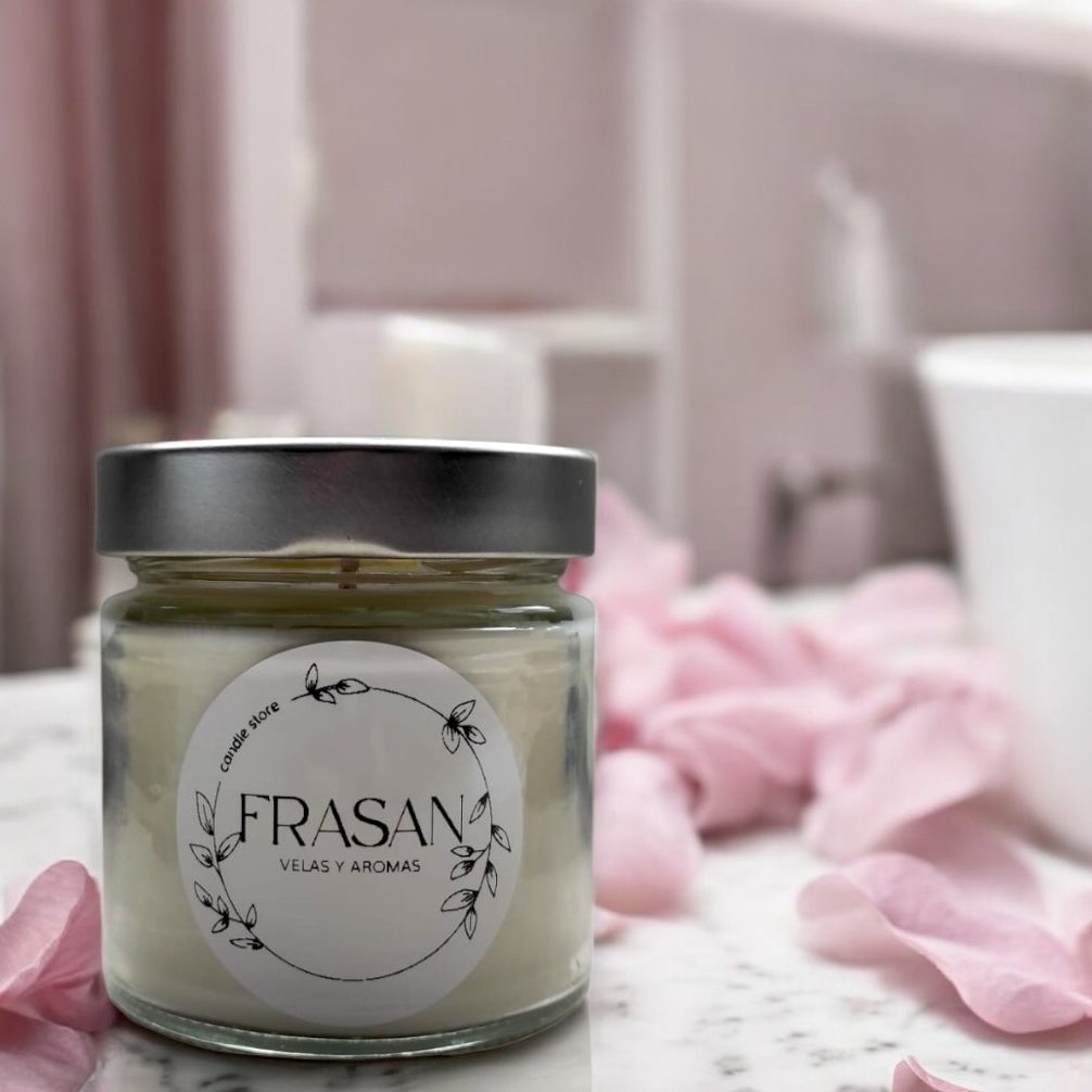 Vela aromática en un frasco de cristal sobre una mesa con pétalos de rosa.