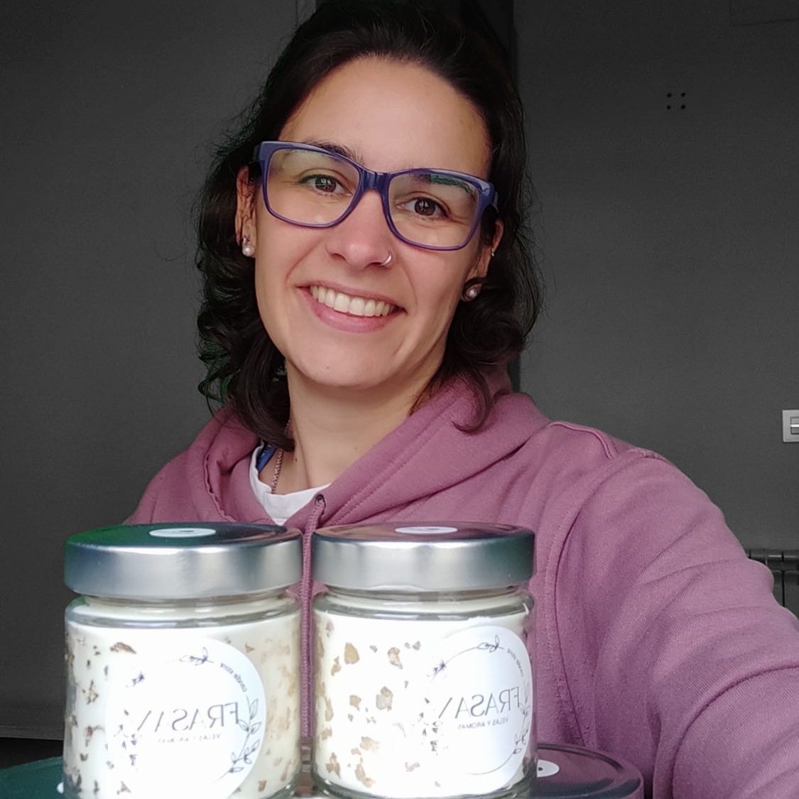 Vela aromática en un frasco sobre una mesa de madera, con libros y una planta de fondo.